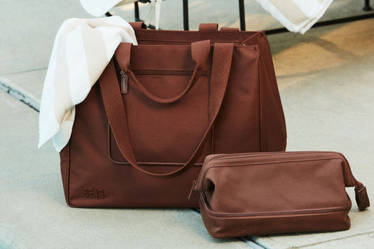Brown weekender bag with a towel hanging out of the bag sitting next to a brown dopp kit